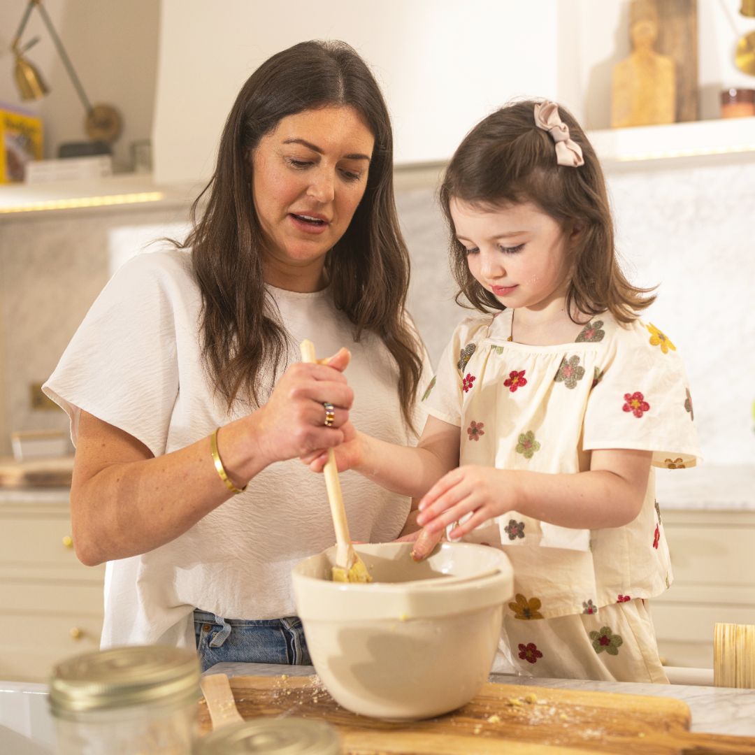  Child helping whisk a baking mix with her mother 