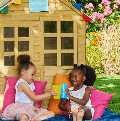 Kids sitting in the garden next to wooden playhouse