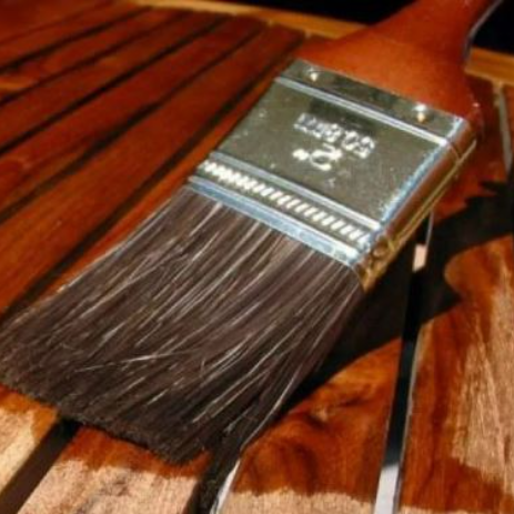 A paintbrush applying wood treatment to a climbing frame