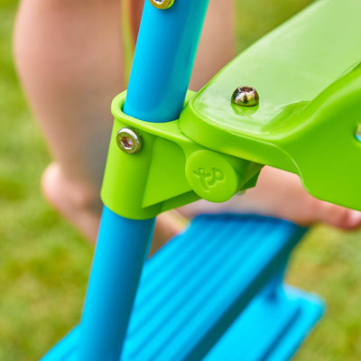 Close-up of a childs bare foot on the TP Toys TP Small to Tall Growable Slides blue and green step ladder, part of an outdoor toy, set on grass.