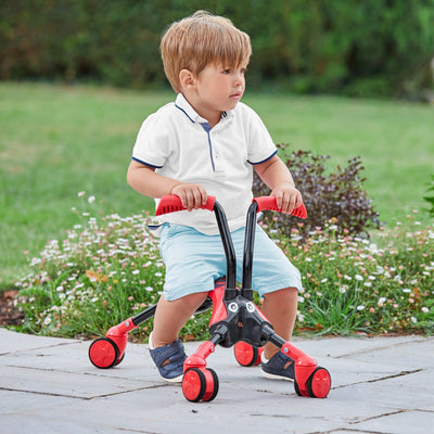 A young child in a white shirt and blue shorts rides the TP Toys ScrambleBug Beetle 4 Wheel Kids Ride On on a stone patio, with grass and plants in the background.