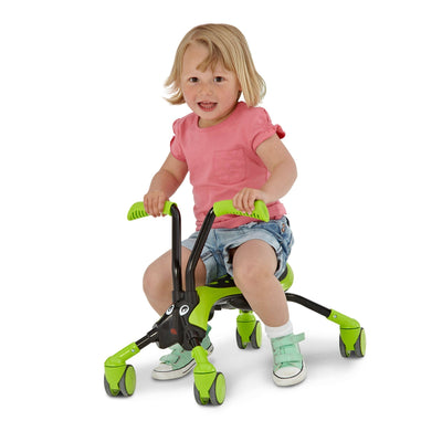 A young child in a pink shirt and denim shorts enjoys 360° movement as they play on the TP Toys ScrambleBug Hornet 4 Wheel Kids Ride On, a green and black toy with four wheels and handlebars.
