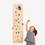 A young girl stands beside The Gruffalo Wooden Height Chart - FSC® certified by TP Toys, decorated with animal illustrations, reaching up to measure her height.