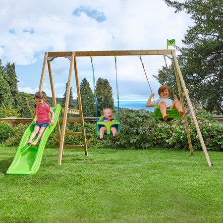 Three children play on the TP Toys Forest Multiplay Double Wooden Swing Set with Quadpod, Roped Rapide seat & Slide—one slides, another swings in the Quadpod baby seat, and the third enjoys the green swing—all outdoors.