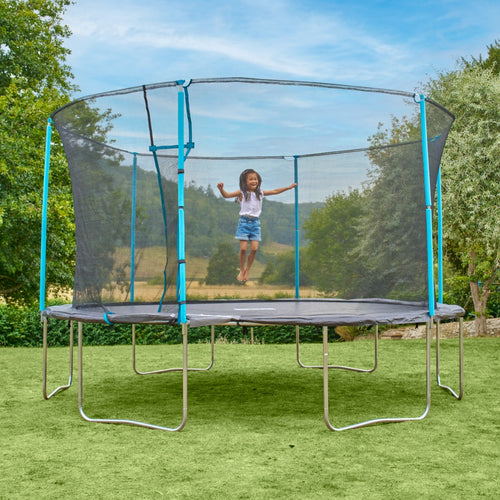 A young girl is jumping on a TP Toys TP Up 14ft Trampoline with a safety net in a grassy backyard on a clear day.
