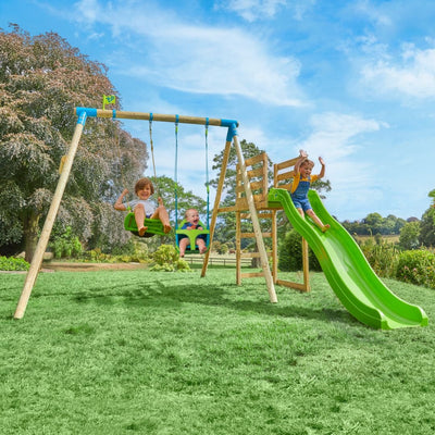 Three children play on the TP Toys TP Kite Wooden Double Swing Set, featuring a quadpod, roped rapide seat, and 8ft slide, set on grass with trees and a blue sky in the background.