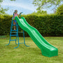 A child stands atop the TP Toys 10ft (3m) Super Wavy Slide & Stepset with blue steps in a grassy backyard, ready for an adventure among tall hedges.