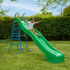 A young child enjoys the TP Toys 10ft (3m) Super Wavy Slide & Stepset in a grassy backyard with hedges and trees in the background.