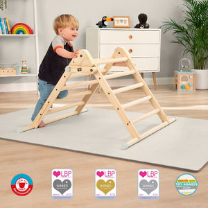 A toddler climbs the TP Toys TP Active-Tots Pikler Style Wooden Climbing Triangle (FSC® certified) in a playroom with a white dresser and toys in the background. Award badges appear at the image's bottom.