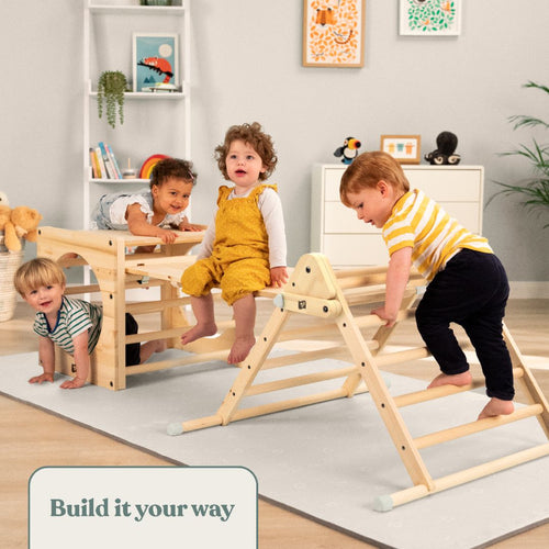 Four young children play and climb on a TP Toys Active-Tots Pikler Style Wooden Climbing Triangle (FSC® certified) and other wooden indoor toys in a brightly lit room with shelves, plants, and framed artwork on the wall.