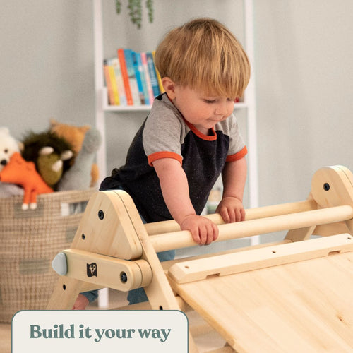 A young child climbs on a TP Toys Active-Tots Pikler Style Wooden Climbing Triangle & Slide (FSC® certified) in a room full of toys and bookshelves. Text at the bottom reads, Build it your way.
