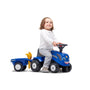 A young child in a white shirt and gray pants sits on the TP Toys Falk New Holland Ride-on Tractor with Trailer, Rake & Shovel—ideal for developing motor skills and encouraging imaginative play.