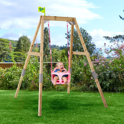 A baby smiles in a pink Quadpod seat, swinging on the TP Toys Forest Acorn Growable Swing Set (FSC® certified) in a grassy backyard garden.