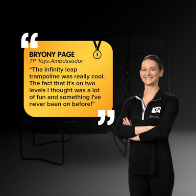 A woman in a black TP Toys top stands smiling with arms crossed beside the TP Infinity® Leap – 2 level Trampoline, sharing how much she enjoys the superior bounce and unique trampoline experience from TP Toys.