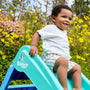 A young child enjoys the TP Toys Bluey Plastic Folding Slide outdoors, surrounded by yellow flowers and greenery.