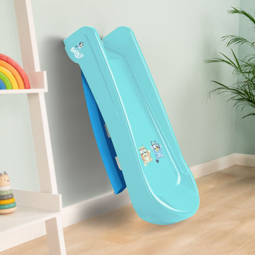 A compact blue TP Toys Bluey Plastic Folding Slide with Bluey characters, set indoors on a wooden floor beside a shelf and a plant.