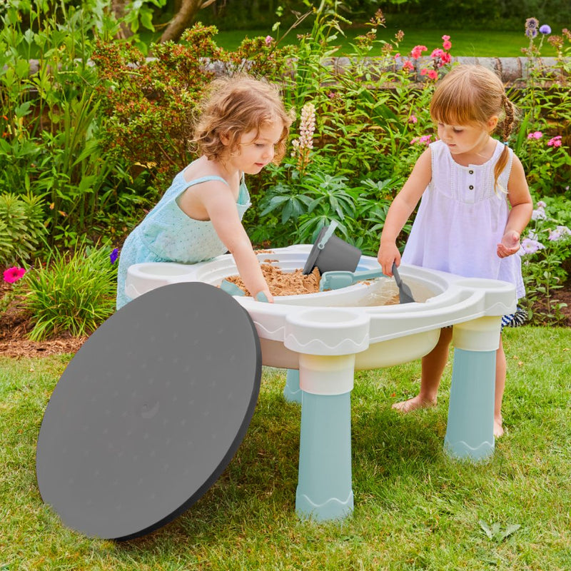 Two young children play with sand in the Palplay Misty Sky Sand & Water Play Table by TP Toys in a garden, its lid resting on the grass nearby.