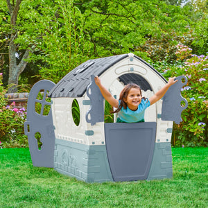 A smiling young child plays with outstretched arms in the TP Toys Palplay Plastic Misty Sky Dream Playhouse, featuring UV resistance and a sunroof, ideal for indoor or outdoor fun on a grassy lawn surrounded by greenery.