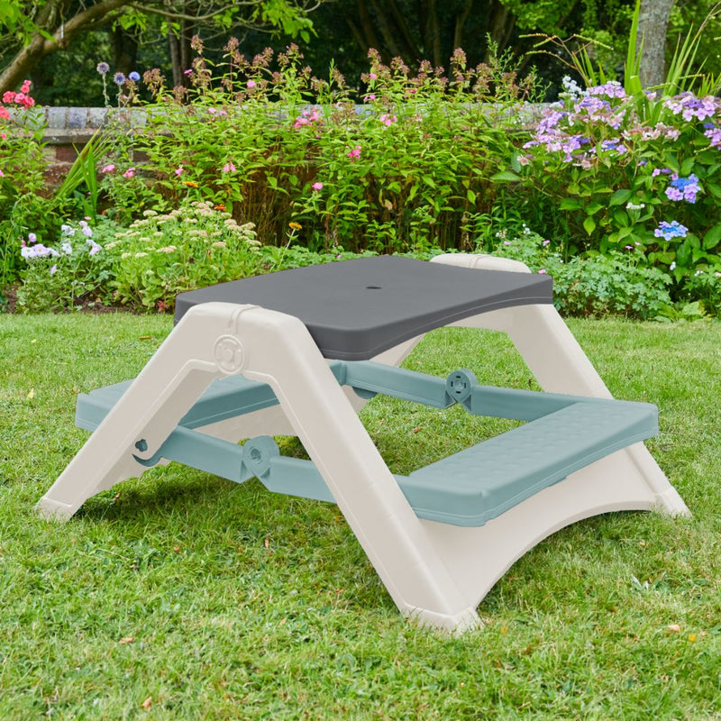The TP Toys Palplay Folding Picnic Bench Misty Sky provides indoor or outdoor seating for kids, perfect for a grass lawn surrounded by flowers and greenery.