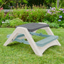The TP Toys Palplay Folding Picnic Bench Misty Sky provides indoor or outdoor seating for kids, perfect for a grass lawn surrounded by flowers and greenery.