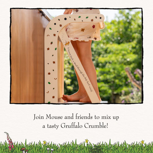 A child stands barefoot on the TP Toys The Gruffalo Wooden Helper Tower – FSC® certified, decorated with animal stickers, reaching up to a kitchen counter.