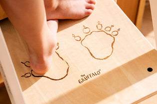A child’s bare feet stand on a step of the TP Toys The Gruffalo Wooden Helper Tower – FSC® certified, featuring etched Gruffalo paw prints and The Gruffalo logo.