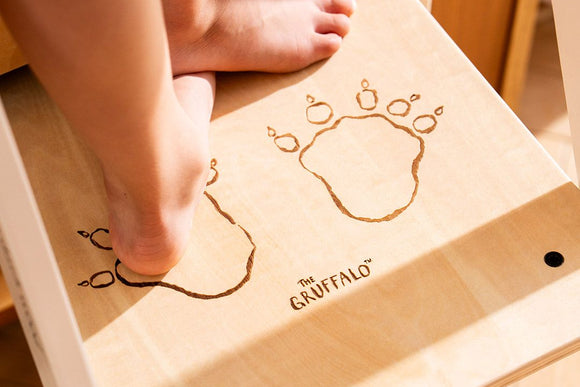 A child’s bare feet stand on a step of the TP Toys The Gruffalo Wooden Helper Tower – FSC® certified, featuring etched Gruffalo paw prints and The Gruffalo logo.