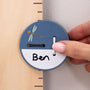 A hand adjusts a round, blue marker labeled Ben on The Gruffalo Wooden Height Chart - FSC® certified by TP Toys, decorated with a small dragonfly illustration.
