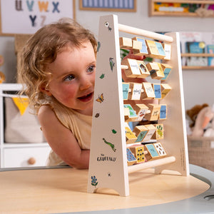 A young child plays with the TP Toys The Gruffalo Wooden Mini Abacus – an FSC® certified early learning toy designed to support fine motor skill development—surrounded by a playroom featuring illustrated alphabet blocks in the background.