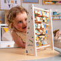 A young child plays with the TP Toys The Gruffalo Wooden Mini Abacus – an FSC® certified early learning toy designed to support fine motor skill development—surrounded by a playroom featuring illustrated alphabet blocks in the background.