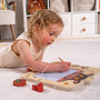 A young child draws on The Gruffalo Wooden Magnetic Drawing Board - FSC® certified by TP Toys, surrounded by toy pieces on the carpet.