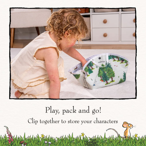 A young child sits on a carpet, placing TP Toys The Gruffalo Play Set wooden characters into a forest-themed storage bag crafted from a double-sided fabric playmat. Text below reads: Play, pack and go! Clip together to store your Gruffalo wooden characters safely inside.