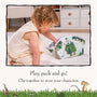 A young child sits on a carpet, placing TP Toys The Gruffalo Play Set wooden characters into a forest-themed storage bag crafted from a double-sided fabric playmat. Text below reads: Play, pack and go! Clip together to store your Gruffalo wooden characters safely inside.