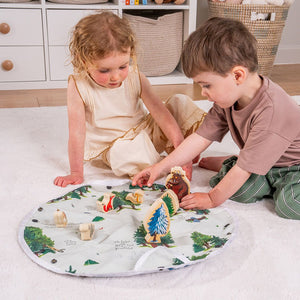 Two young children sit on a white carpet, playing with the TP Toys The Gruffalo Play Set with Wooden Characters on a round, double-sided fabric playmat in a tidy room.