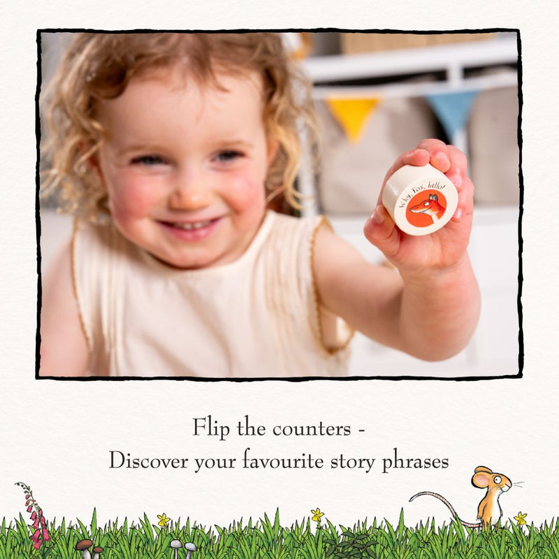 A young child holds up a colorful counter from the TP Toys The Gruffalo Wooden Counting Clock—FSC® certified—and smiles at the camera. This engaging clock encourages early numeracy as children turn the counters to reveal their favorite phrases from The Gruffalo story.