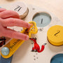 A child’s hand spins the yellow wooden clock hand on The Gruffalo Wooden Counting Clock - FSC® certified by TP Toys—a circular counting toy adorned with numbers and animal illustrations, such as a fox and mouse—making it perfect for fostering early numeracy skills.