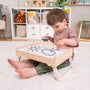 A young boy sits on the floor in the playroom, coloring a drawing of a sun and cloud on his TP Toys The Gruffalo Wooden Creative Station – FSC® certified, surrounded by magnetic pieces and other wooden creative toys.