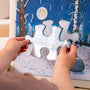 A person holds a puzzle piece and gets ready to fit it into a winter scene jigsaw featuring snowy trees, a moon, and a birch tree—much like the creative fun kids can enjoy with the TP Toys Gruffalo Wooden Creative Station - FSC® certified, which uses magnetic pieces for hours of imaginative play.