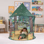 A young child lounges inside the TP Toys The Gruffalo Play Tent, adorned with delightful illustrations from The Gruffalo, in a cozy, book-filled playroom—perfect for imaginative play.