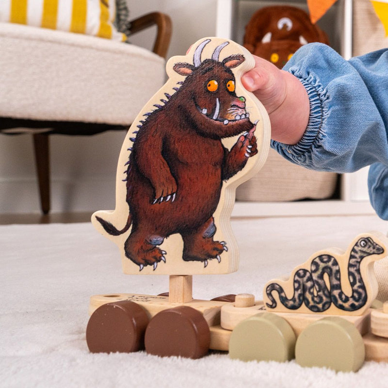 A child holds The Gruffalo Wooden Pull Along Character Set by TP Toys, FSC® certified, with the charming figures nearby on the floor in a cozy room—sparking imaginative play.
