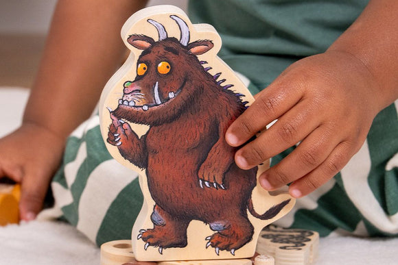 A child enjoys imaginative play with the TP Toys The Gruffalo Wooden Pull Along Character Set - FSC® certified, rolling the toy on a white surface while wearing green and white striped pants.