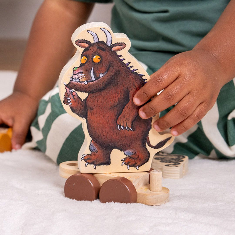 A child enjoys imaginative play with the TP Toys The Gruffalo Wooden Pull Along Character Set - FSC® certified, rolling the toy on a white surface while wearing green and white striped pants.