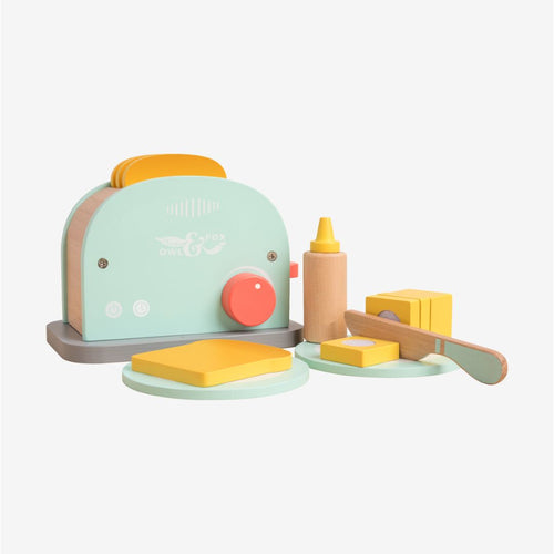 The TP Toys Owl & Fox Wooden Toaster Set - FSC® certified, in soothing pastel colors, includes bread slices, butter, a knife, and a bottle artfully arranged on a light background. This charming Montessori toy inspires pretend play and encourages imaginative kitchen adventures.