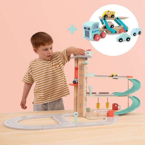 A young boy enjoys playtime with the TP Toys Owl & Fox Wooden Multi-storey Garage with Vehicle Transporter (FSC® certified) on a table, as extra vehicles and pretend play accessories appear in a bubble overhead.
