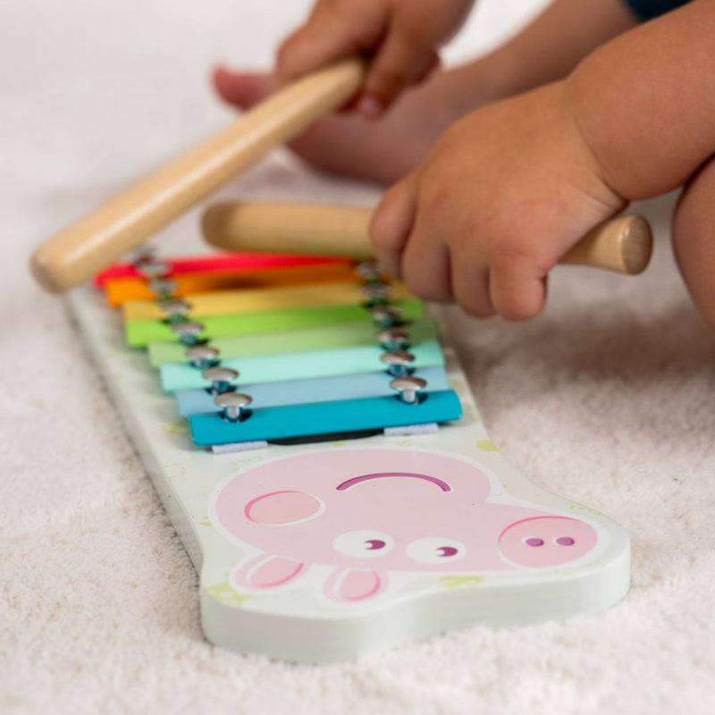 A child enjoys building early musical skills with the TP Toys Grow With Peppa Pig Wooden Xylophone and mallets on a white carpet.