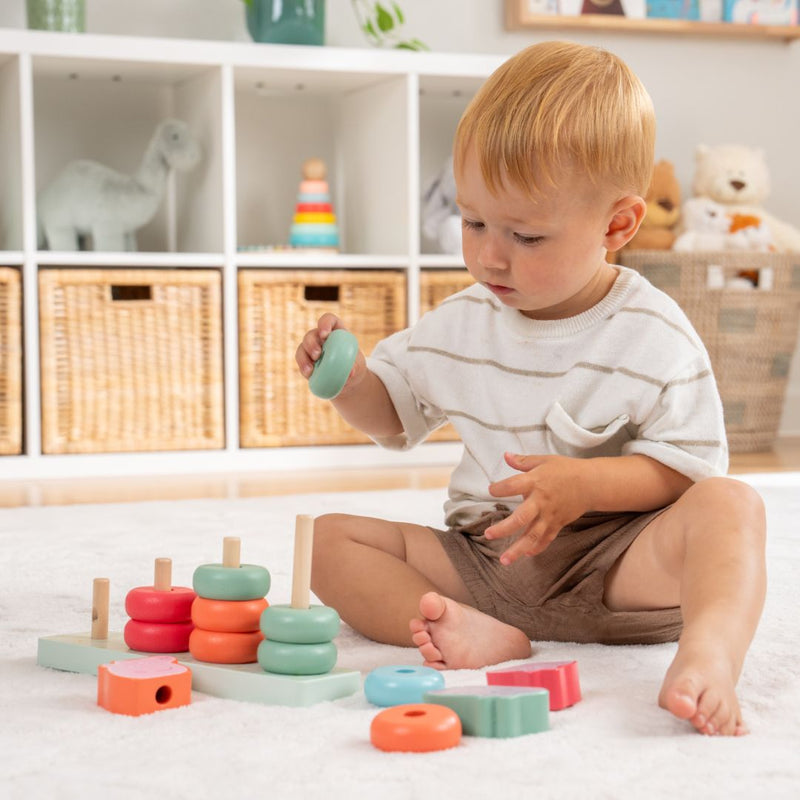 A young child builds fine motor skills by stacking colorful rings on the TP Toys Grow with Peppa Pig Wooden Family Ring Stacker in a bright, organized playroom.