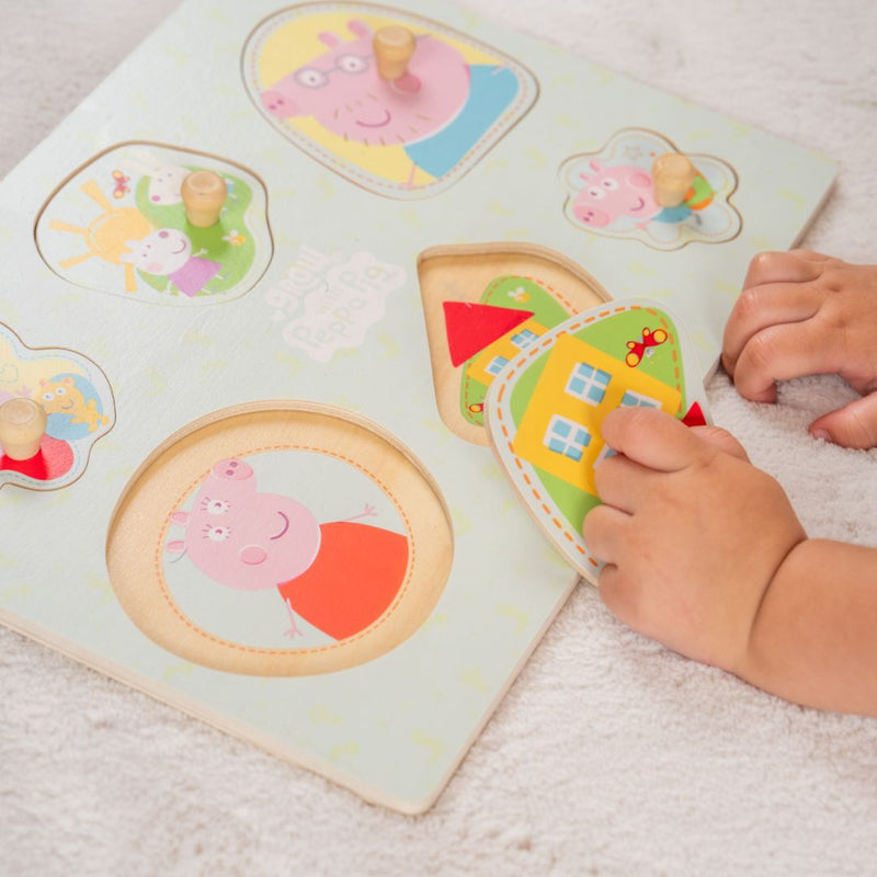 A child assembles the TP Toys Grow with Peppa Pig Wooden Puzzle Set, featuring Peppa Pig characters and house shapes on a white surface, helping to develop fine motor skills and hand-eye coordination.