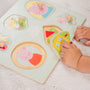 A child assembles the TP Toys Grow with Peppa Pig Wooden Puzzle Set, featuring Peppa Pig characters and house shapes on a white surface, helping to develop fine motor skills and hand-eye coordination.