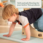 A young child plays on TP Active-Tots Premium Play Safety Mats by TP Toys next to a wooden climbing structure, showing safe, non-toxic flooring for play. Text above reads: Soft and safe flooring for your Active-Tots products.