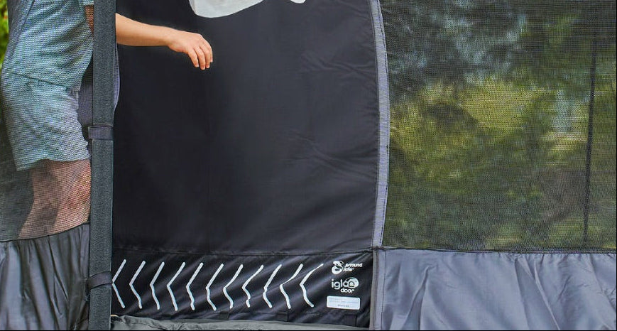 A child enters the TP Toys TP Genius® 8ft Round Trampoline through its zippered mesh door, set outdoors among lush greenery, highlighting trampoline safety in action.